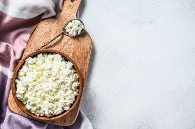 Tahta kesme tahtasındaki ahşap kasede taze süzme peynir. Gri arka plan. Üst Manzara. Boşluğu kopyala