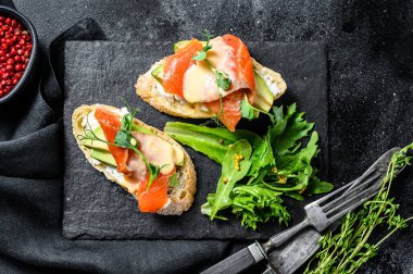 Avokado ve somonlu sağlıklı sandviç. Ispanak ve roka salatası. Siyah arka plan. Üst görünüm.