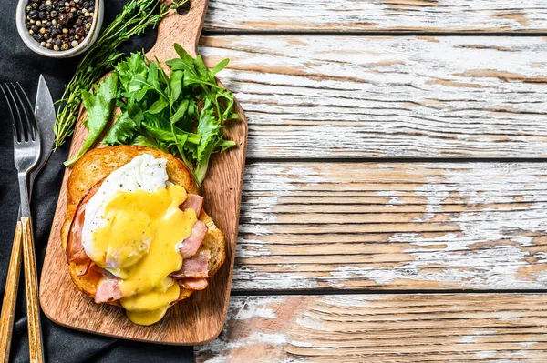 Breakfast Burger with bacon, egg Benedict, hollandaise sauce on brioche bun. Garnish with arugula salad. White background. Top view. Copy space.