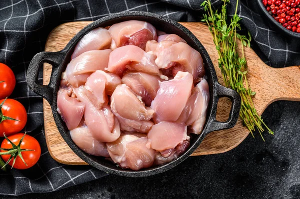 Sliced chicken thighs fillet without skin in a pan. Black background. Top view.