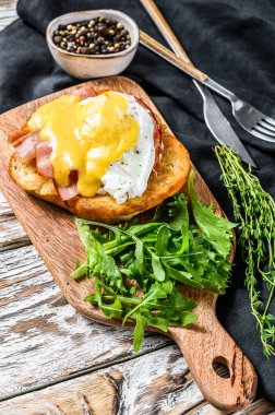 Pastırmalı kahvaltı burgeri, Benedict yumurtası, brioche ekmeğine Hollandaise sosu. Arugula salatalı garnitür. Beyaz arka plan. Üst görünüm.