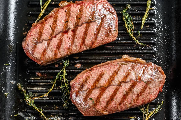 Grilled meat Top Blade steaks in a frying pan. Gray background. Top view.