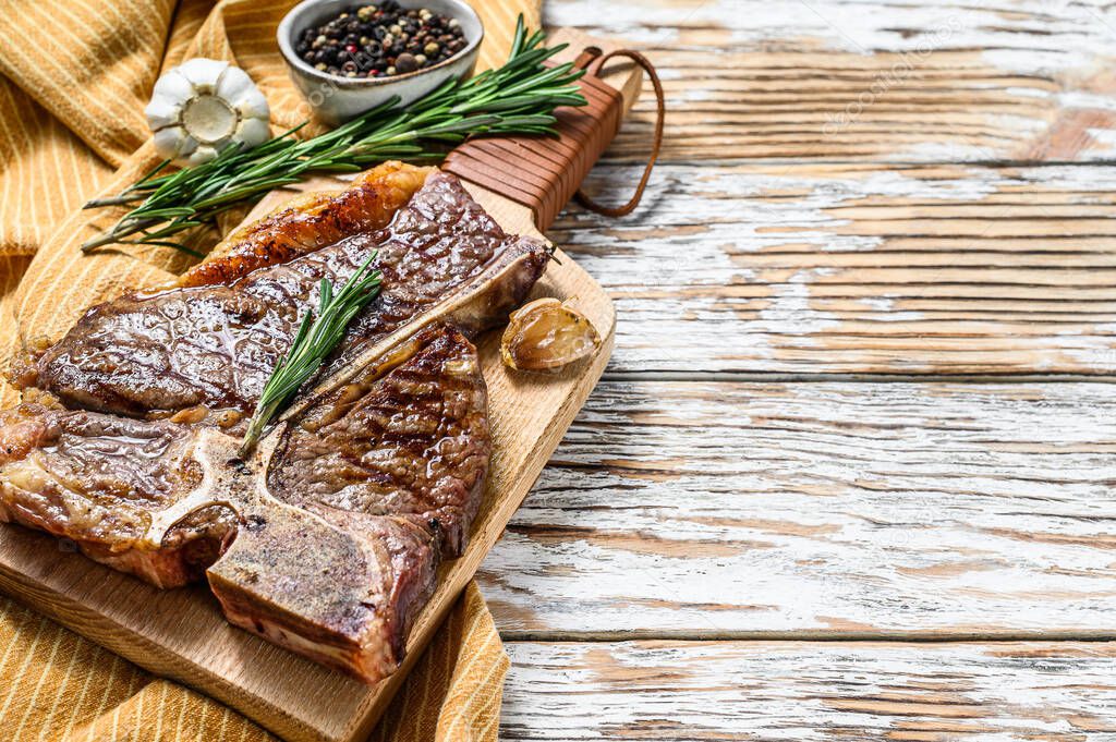 Grilled Porterhouse steak on a chopping Board. Cooked beef meat. White wooden background. Top view. Copy space.