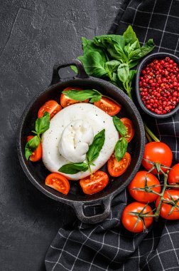 Burrata mozzarella, vişneli domates ve fesleğenli Caprese salatası. Siyah arka plan. Üst görünüm.