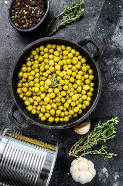 Kızartma tavasında konserve yeşil bezelye. Konserve yiyecekler. Siyah arka plan. Üst görünüm.