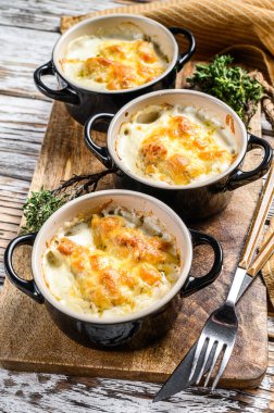 Julienne, ahşap bir masada porsiyon şeklinde tavuk ve peynirle. Beyaz arka plan. Üst görünüm.