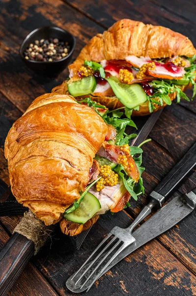 Croissant filled with ham and lettuce on wooden chopping board. Black background. Top view.