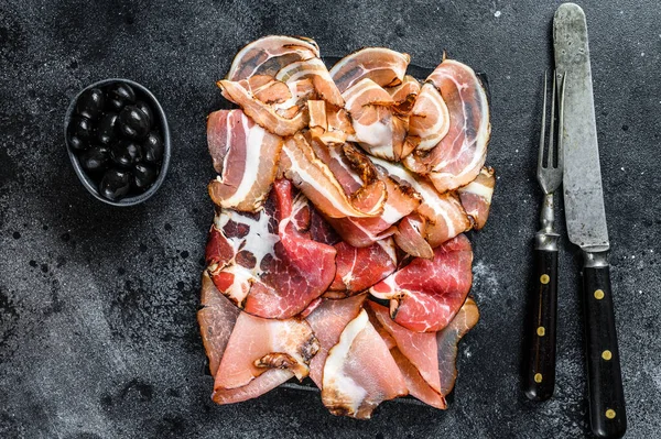 Meat antipasto platter, pancetta, salami, sliced ham, sausage, prosciutto, bacon. Black background. Top view.