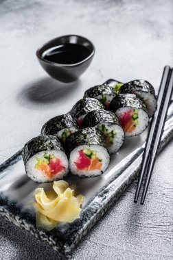 Suşi somon, avokado ve ton balıklı hosomaki sarıyor. Gri arka plan. Üst görünüm.