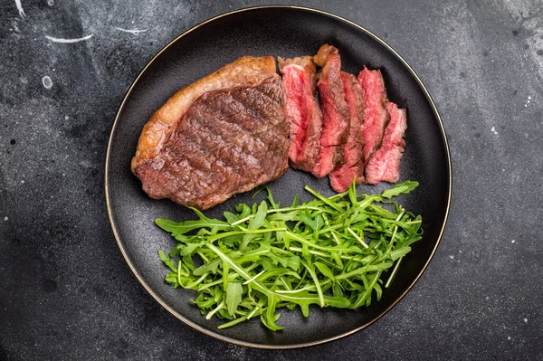 Appetizing grilled striploin steak with salad, inviting you to indulge in a mouthwatering culinary experience. black background. top view.