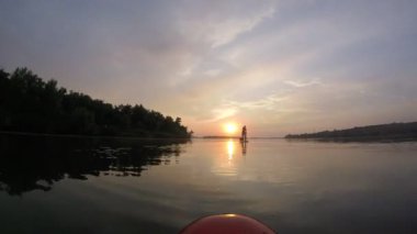 Sup tahtasında kürek çekmek. Güneşin arka planında sup tahtası. Sunrise. Bir adam güneşin şafağında Sup tahtasında kürek çekiyor. Gökyüzünün ve bulutların su üzerindeki yansıması.