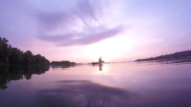 Sup tahtasında kürek çekmek. Güneşin arka planında sup tahtası. Sunrise. Bir adam güneşin şafağında Sup tahtasında kürek çekiyor. Gökyüzünün ve bulutların su üzerindeki yansıması.