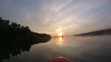 Sup tahtasında kürek çekmek. Güneşin arka planında sup tahtası. Sunrise. Bir adam güneşin şafağında Sup tahtasında kürek çekiyor. Gökyüzünün ve bulutların su üzerindeki yansıması.
