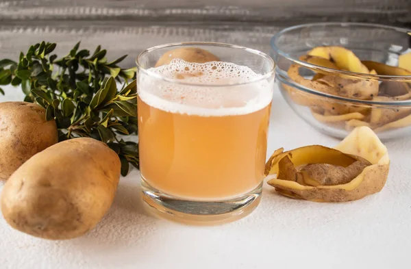 Patates suyu bir bardak bütün patates ve skarlupa yakın.
