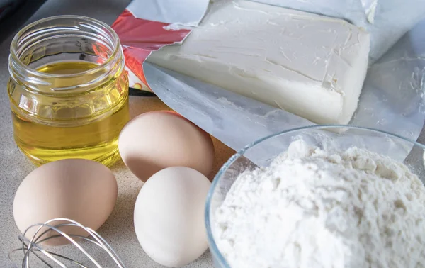 Zutaten zum Kochen. Mehl und Zucker in einem Glasbehälter, Eier und Butter auf einem weißen Tisch. — Stockfoto