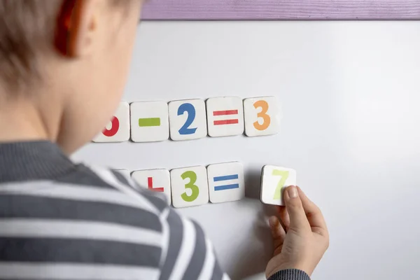 A little boy solves a difficult task. Against the background of the school board with numbers in their hands.