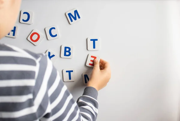 A child learns the letters on the blackboard. The boy is studying the letters.