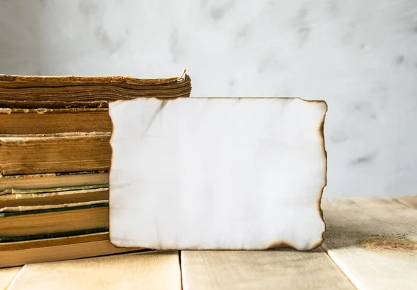 Livros antigos em cima da mesa. Uma folha de papel branca queimada ao redor das bordas. Lugar para o seu texto . — Fotografia de Stock