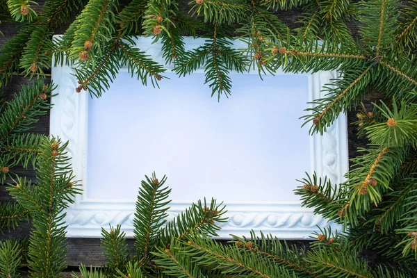 古い木の板の背景にクリスマスツリーの白いフレームと緑の枝。コピースペース付きのトップビュー — ストック写真