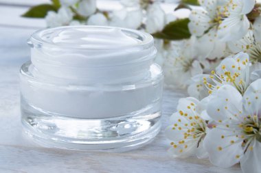 Bir kavanoz krem yakın çekim, kiraz çiçekleri ile çevrili yüz kremi.