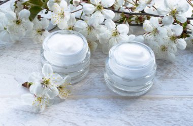 Beyaz bir arka planda beyaz teneke kutu, kozmetik krem ve kiraz çiçekleri.