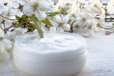 Beyaz bir arka planda beyaz teneke kutu, kozmetik krem ve kiraz çiçekleri.