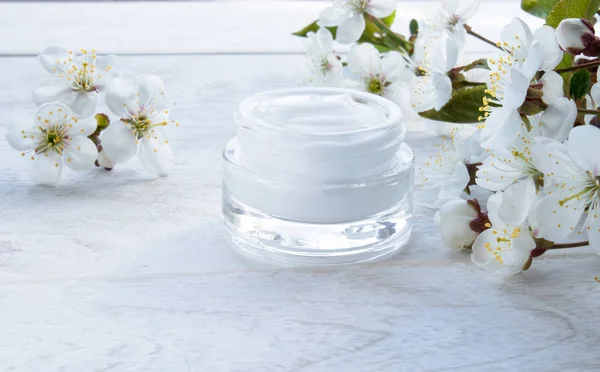 Lata blanca, crema cosmética y flores de cereza sobre un fondo blanco . — Foto de Stock