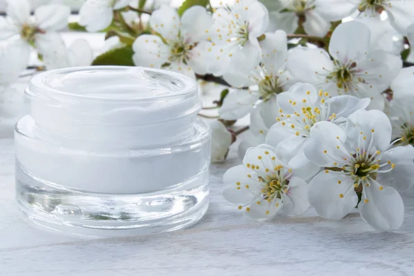 Lata blanca, crema cosmética y flores de cereza sobre un fondo blanco . — Foto de Stock