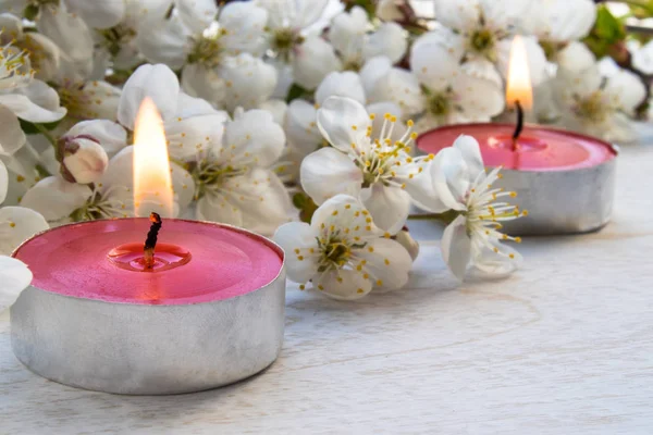 Velas de cera están ardiendo cerca de las ramas de la cereza en flor en la mesa . —  Fotos de Stock