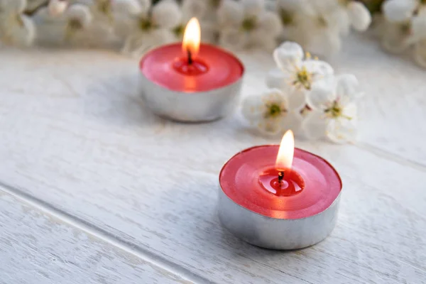 Una vela está sobre una mesa blanca de madera cerca de las ramas de flores blancas de cerezo . —  Fotos de Stock