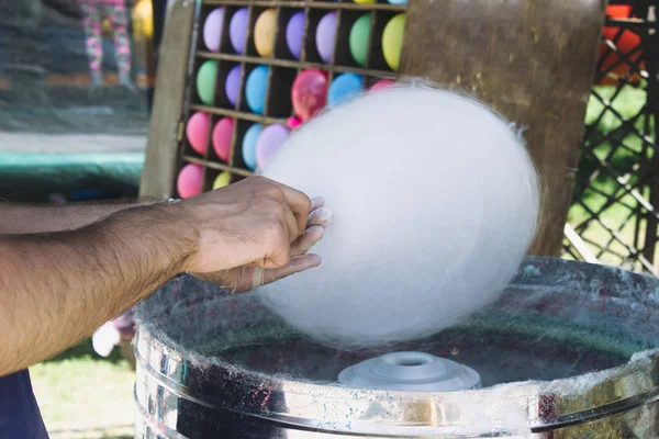 A hand wrap a cotton candy on a stick in a cotton candy machine.