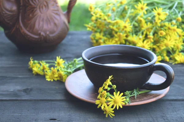 Чайник и чашка чая стоят на деревянных старых досках с желтыми цветами маргаритки. С копировальным местом . — стоковое фото