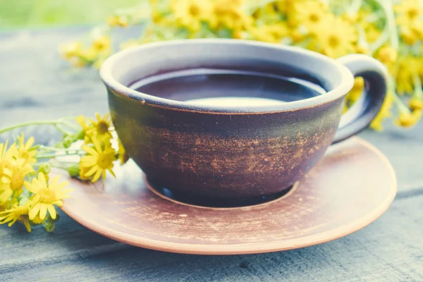 Чашка чая из желтых маргариток с букетом маргариток на деревянном фоне . — стоковое фото