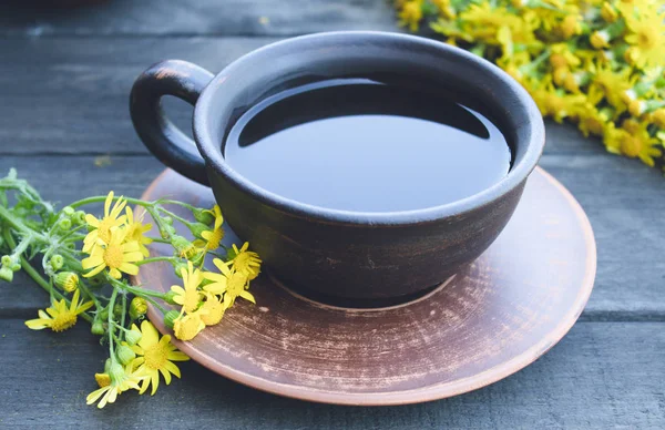 Чашка чая из желтых маргариток с букетом маргариток на деревянном фоне . — стоковое фото