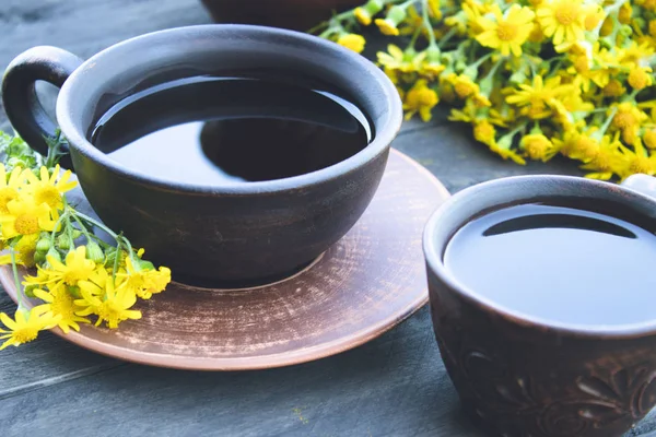 Две чашки чая стоят на деревянных старых досках с желтыми ромашками . — стоковое фото