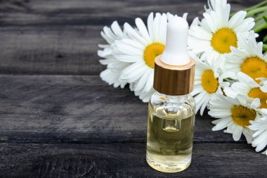 Bir pipet ile cam şişede Papatya uçucu yağ papatya çiçekleri yakınında masada.