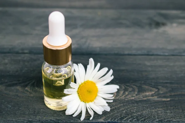 Chamomile essential oil in a glass bottle with a pipette stands on the table near the chamomile. — Stock Photo, Image