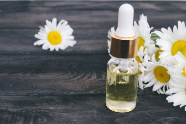 Bir pipet ile cam şişede Papatya uçucu yağ papatya çiçekleri yakınında masada.