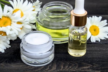 Uçucu yağ ve kozmetik krem beyaz papatya çiçekleri yakınında ahşap bir masada.