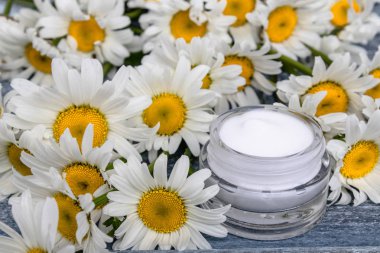 Cam bir kavanozda kozmetik krem papatyalar yakınında duruyor.