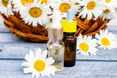 Bir cam şişe papatya esansiyel yağ papatya çiçekleri ile sepet yakınında ahşap panoları üzerinde duruyor.