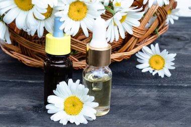 Bir cam şişe papatya esansiyel yağ papatya çiçekleri ile sepet yakınında ahşap panoları üzerinde duruyor.