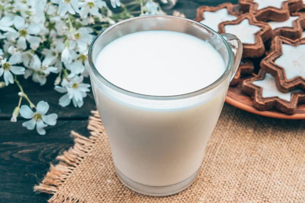 Junto a la galleta y las flores blancas hay una taza de leche en una servilleta . — Foto de Stock