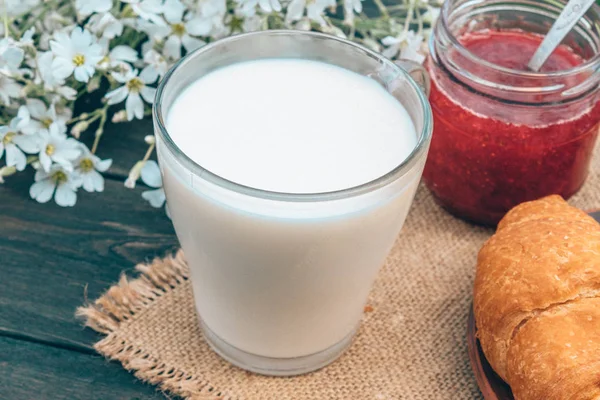 Junto a los croissants y las flores blancas hay una taza de leche . — Foto de Stock