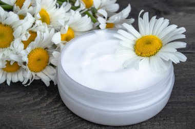 ahşap bir masada papatya çiçekleri yakınında kozmetik krem