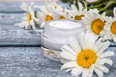Cam bir kavanozda kozmetik krem papatyalar yakınında duruyor.