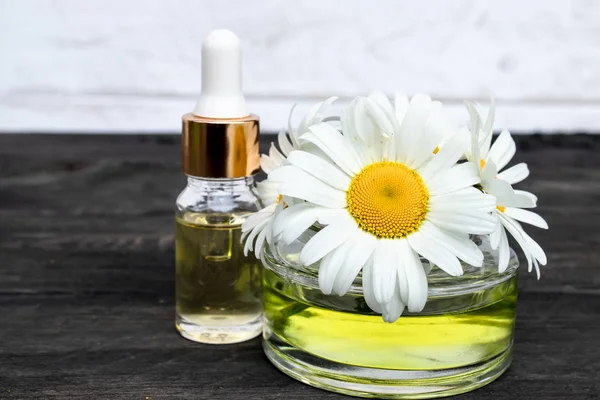 Ätherisches Kamillenöl in einem Glas in Großaufnahme auf einem Tisch mit Gänseblümchen und einer Flasche Öl. — Stockfoto