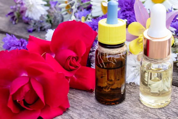 Huile essentielle avec une rose dans une bouteille en verre près de fleurs sauvages sur fond en bois . — Photo