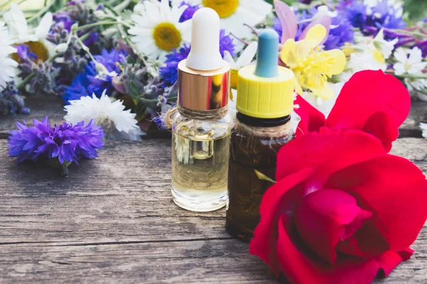 Эфирное масло с розой в стеклянной бутылке возле полевых цветов на деревянном фоне . — стоковое фото