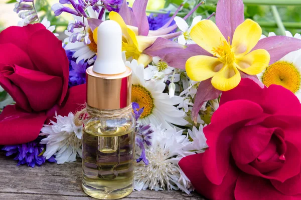 Minyak esensial dalam botol kaca dekat bunga liar dengan latar belakang kayu . — Stok Foto
